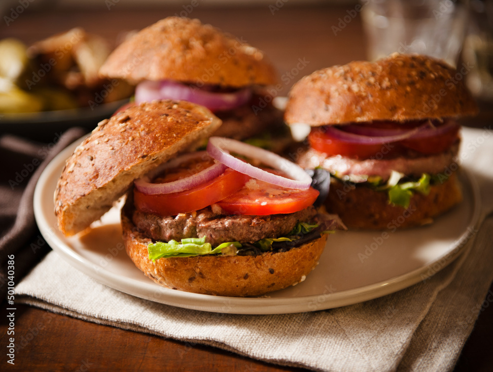 Three Burgers with Lettuce Onion and Tomato on a Platter Three Burgers with Lettuce Onion and Tomato on a Platter