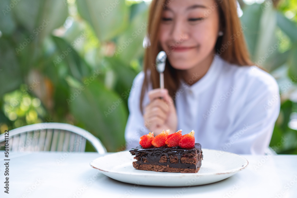 A beautiful young asian woman eating a piece of strawberry chocolate cake