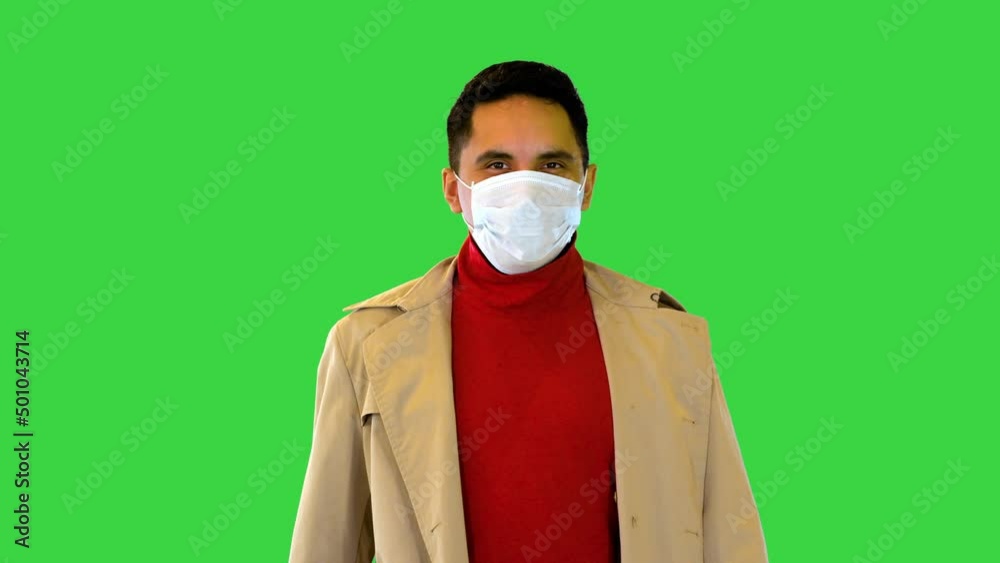 Latin man happy smiling under protective medical face mask for covid prevention walking wear trench on a Green Screen, Chroma Key. Latin man happy smiling under protective medical face mask for covid prevention walking wear trench on a Green Screen, Chroma Key.