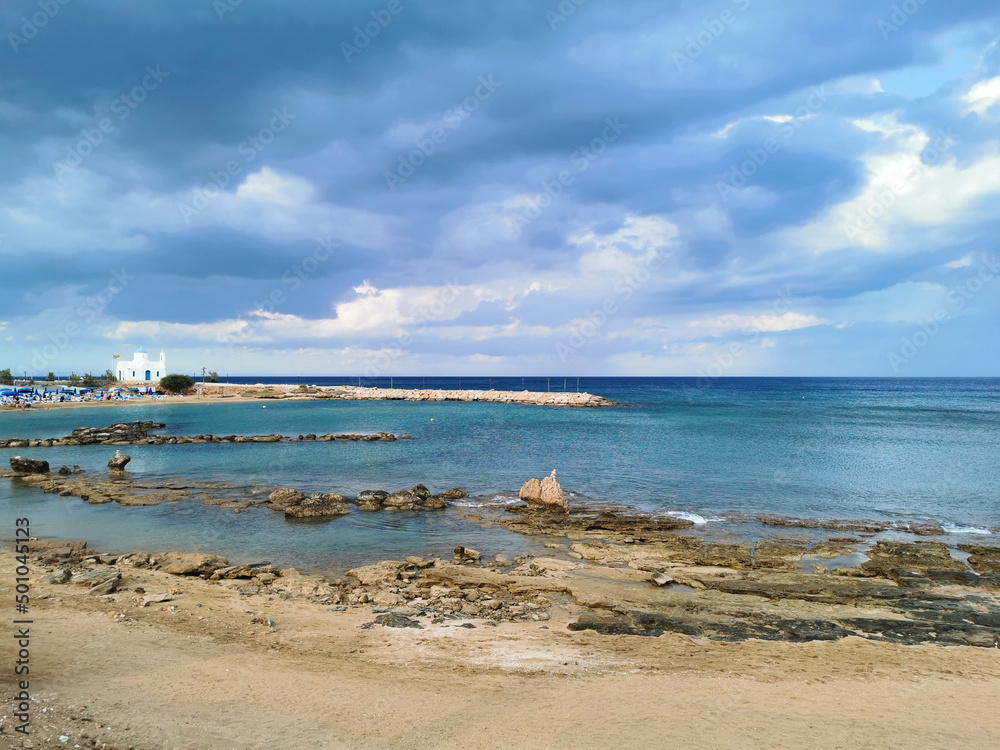 Rocky shore with sand, sandy beach, the temple of St. Nicholas the Wonderworker against the backdrop of a dramatic sky.