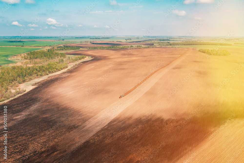 Aerial view, Top View Tractor Plowing Field In Spring Season. Beginning Of Agricultural Spring Season. Cultivator Pulled By A Tractor In Countryside Rural Field Landscape.