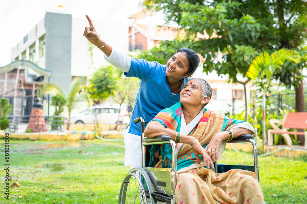 Obraz premium Nurse showing nature and birds to senior women while sitting on wheelchair at park - concept of relaxation, healthcare treatment and rehabilitation.