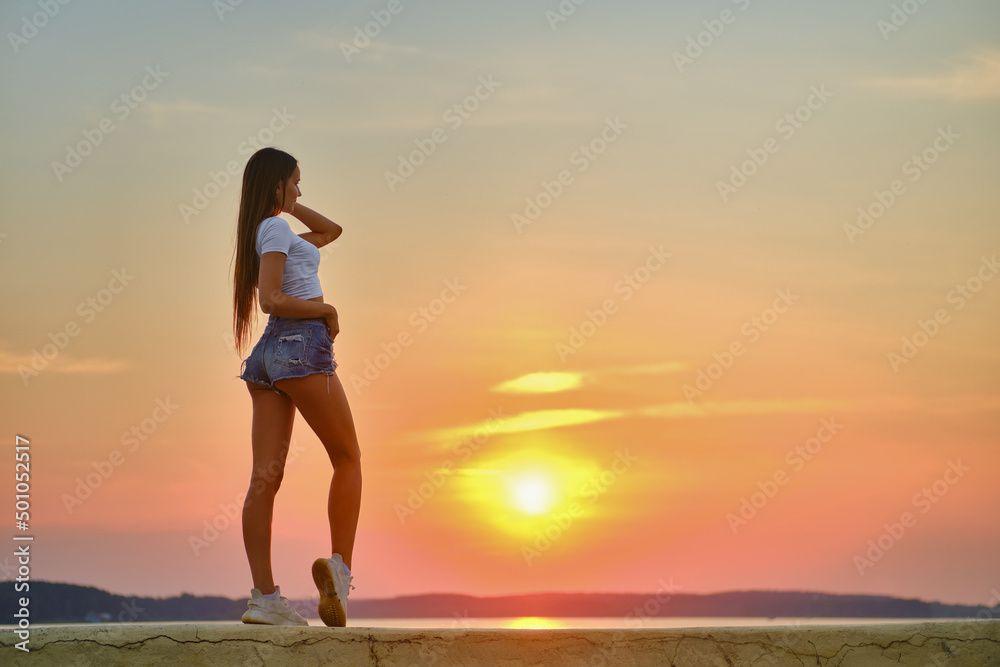 Young woman stands on a pier and looking at the sunset