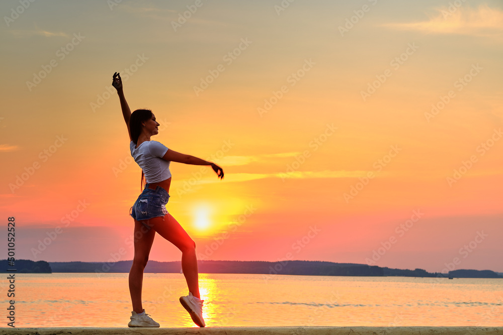 Side view of young woman stands on a pier during the sunset