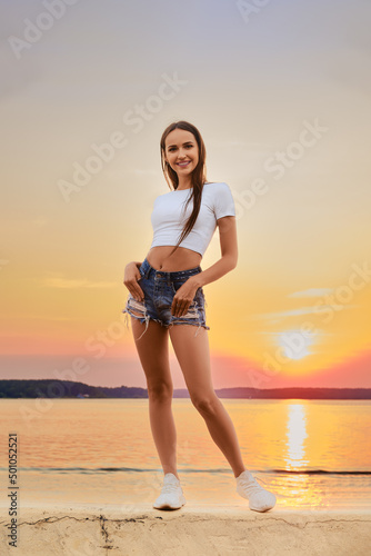 Joyful woman in tee shirt and shorts posing on a pier over the sunset