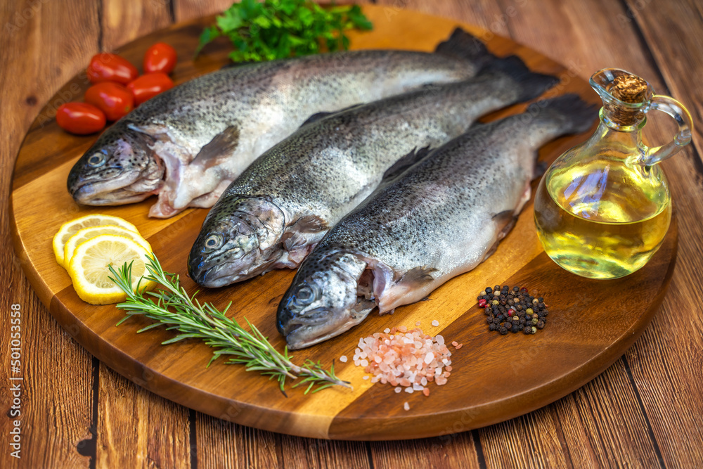 Three raw trout with spices and olive oil on a wooden board. Three raw trout with spices and olive oil on a wooden board.