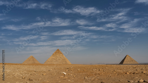 The three great pyramids of Giza - Cheops  Khafre  Menkaur - against the blue sky and clouds. In the foreground is a rocky-sandy desert. Silhouettes of Cairo buildings on the horizon. Egypt