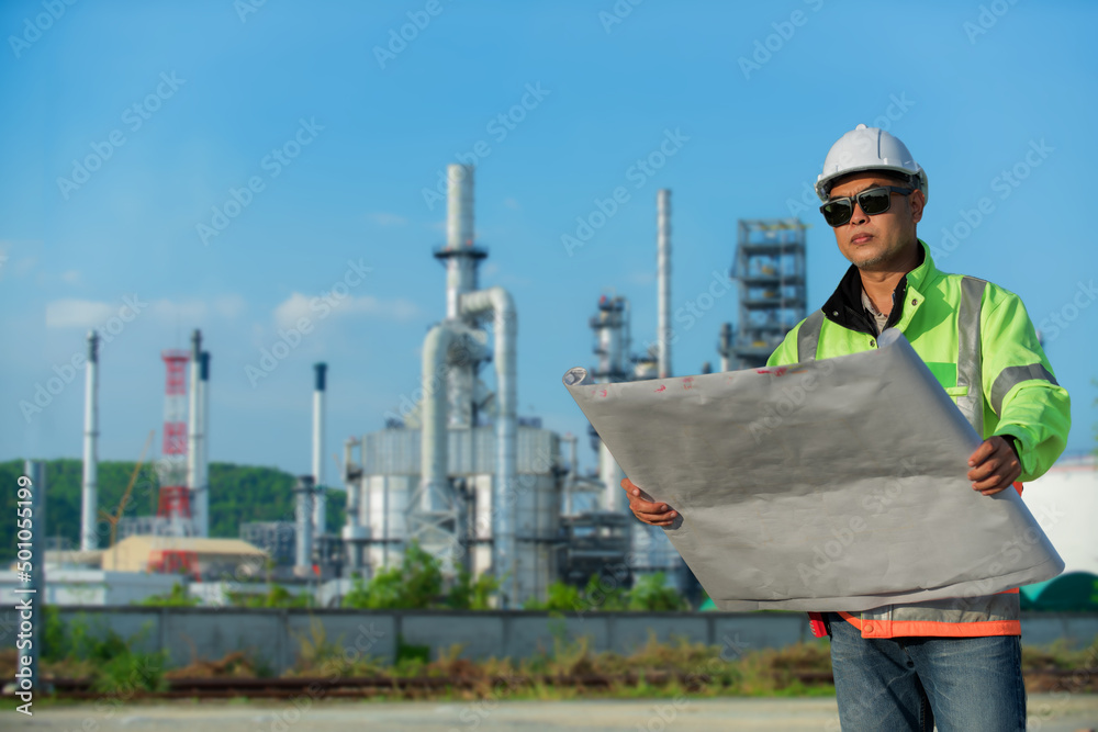 worker holding a blueprint. worker with helmet. Refinery industry engineer wearing PPE with hand hold drawing working at refinery construction site. worker holding a blueprint. worker with helmet. Refinery industry engineer wearing PPE with hand hold drawing working at refinery construction site.
