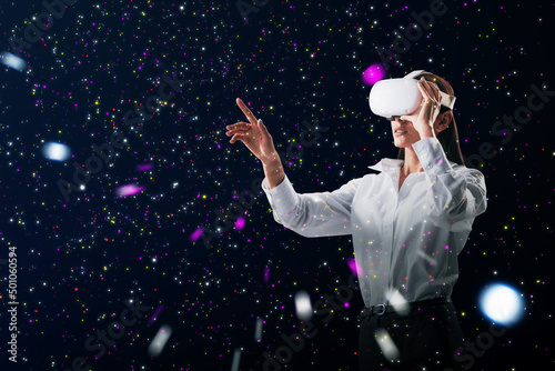 Abstract double exposure image of attractive young white european woman with VR glasses pointing at starry sky space background. Metaverse, future and wearable device concept.