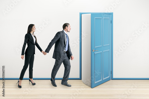 Thoughtful european businessman and businesswoman looking at creative open blue book door in concrete interior. Education, knowledge, opportunity and success concept.