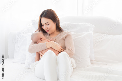 Selective focus Beautiful Asian mother holding newborn baby and looking at baby with love and showing protection. Mom and adorable infant spend time together at home.