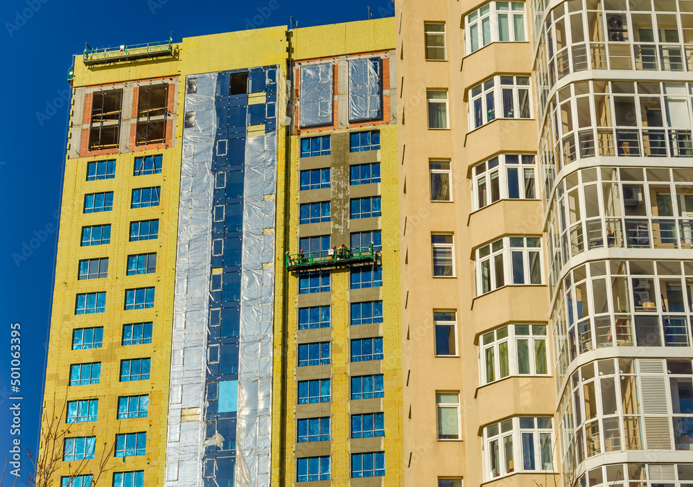 Fototapeta premium Workers on a cradle repair a tall house.