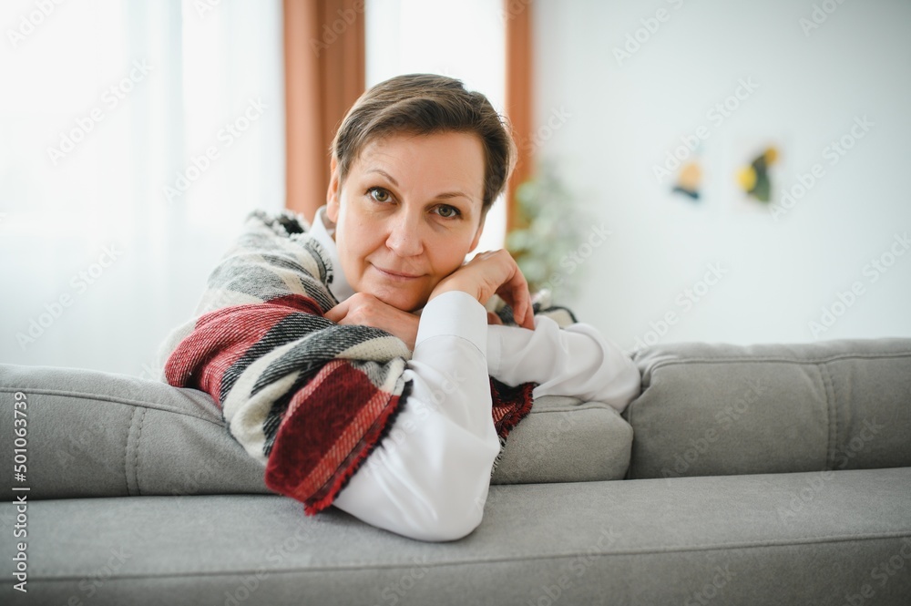 Mature Woman. Beautiful Healthy Middle Age Female Sitting On Sofa At Home. Beauty And Comfort Concept. Mature Woman. Beautiful Healthy Middle Age Female Sitting On Sofa At Home. Beauty And Comfort Concept.
