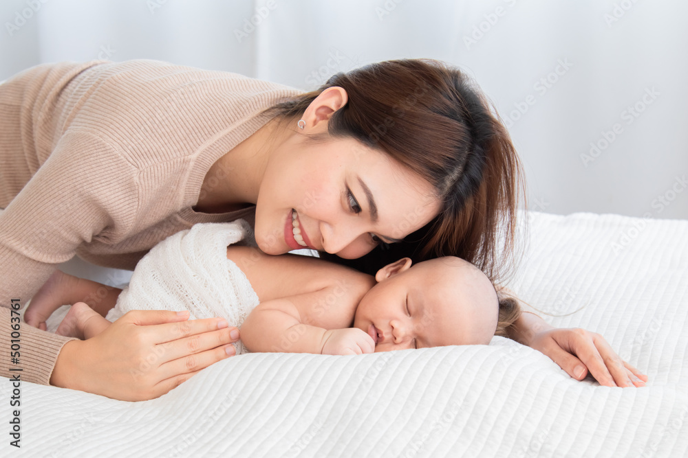Beautiful asian mom supports and tenderly cuddles newborn baby gently while baby deepy sleeping on bed. Young woman looking adorable infant with love and tender. Mother and child spend time together. Beautiful asian mom supports and tenderly cuddles newborn baby gently while baby deepy sleeping on bed. Young woman looking adorable infant with love and tender. Mother and child spend time together.