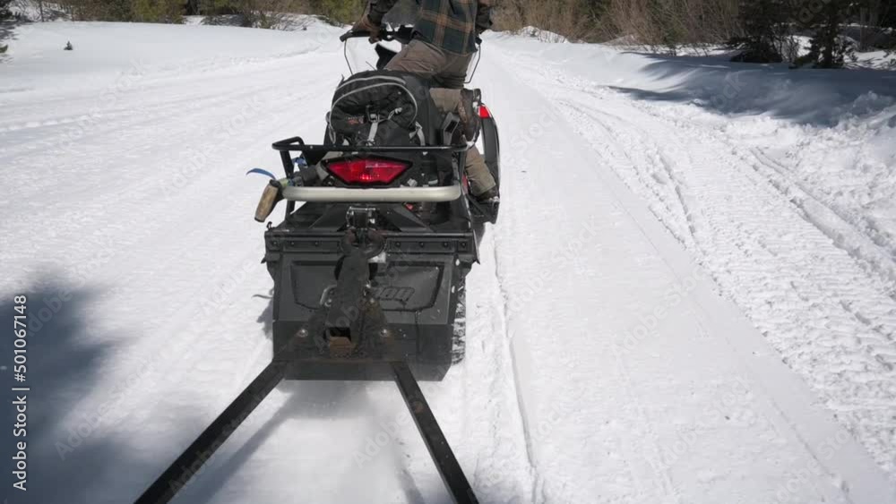 Snowmobile tracks kicking up loose snow onto passengers riding behind it Snowmobile tracks kicking up loose snow onto passengers riding behind it