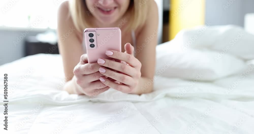 Smiling woman is texting in a smartphone while lying in bed