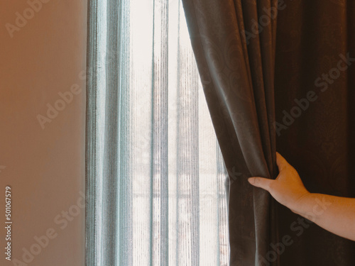 woman's hand opening brown luxurous curtain photo