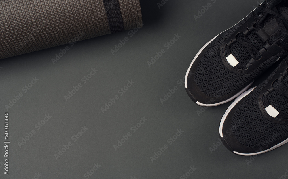 Fitness mat and black sneakers on a dark grey background. Top view, space for text. Fitness mat and black sneakers on a dark grey background. Top view, space for text.