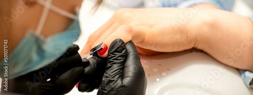 Professional manicure. A manicurist is painting the female nails of a client with red nail polish in a beauty salon  close up. Beauty industry concept