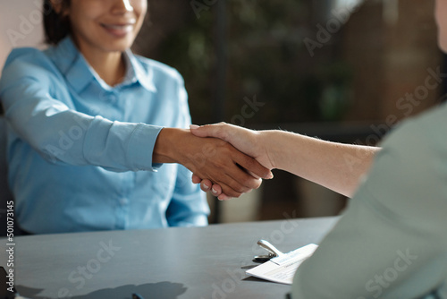 Close-up of young woman shaking hands with employer at table during meeting at office