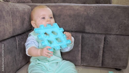 baby sits on floor and chews on a plastic toy