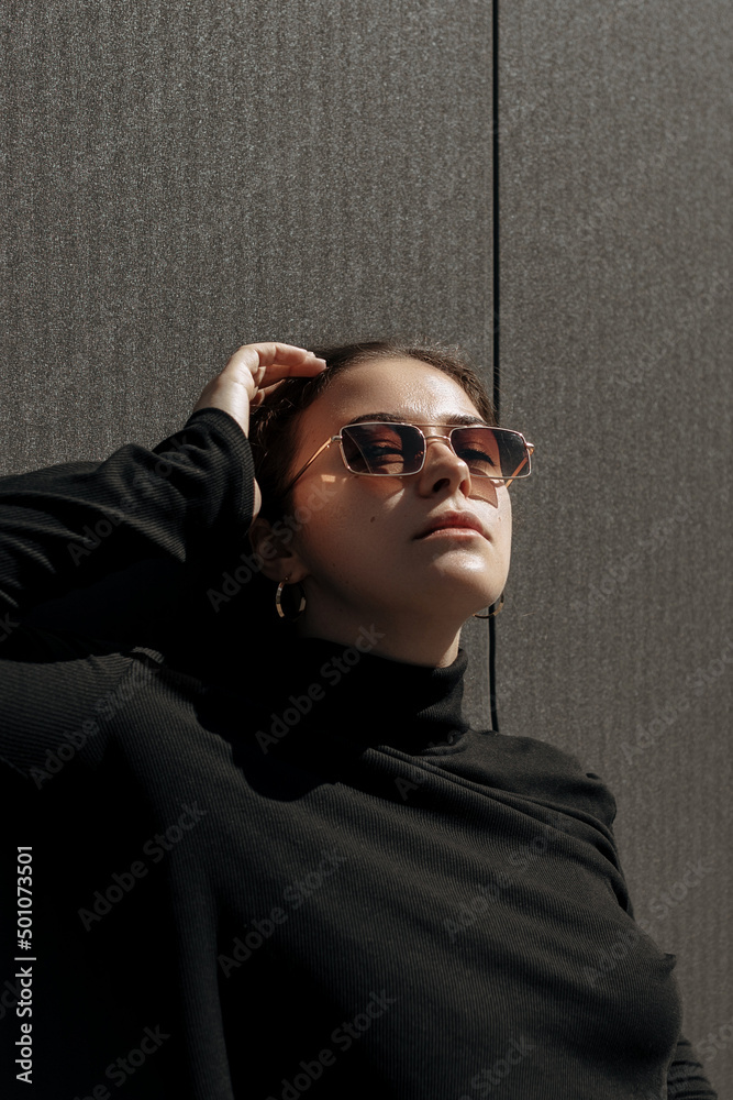 Pretty female model in black pullover posing on the wall background in sun rays Pretty female model in black pullover posing on the wall background in sun rays