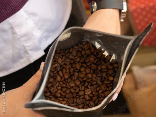 Female hands hold an open black bag with coffee roasted beans in the store. Coffee retail concept