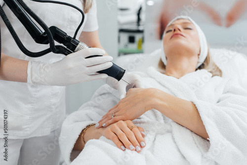 A young girl gets carbon peeling for the skin of her hands in a beauty salon. Laser pulses cleanse the skin. Hardware cosmetology. The process of photothermolysis, warming the skin.