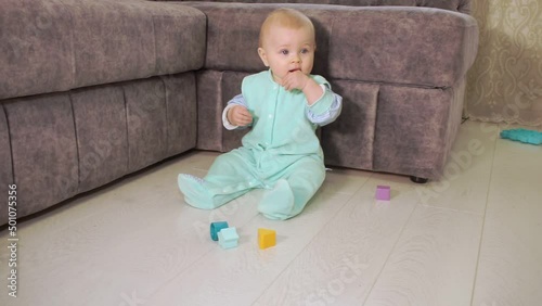 baby in turquoise suit sits on floor, then smiles and crawls out of frame