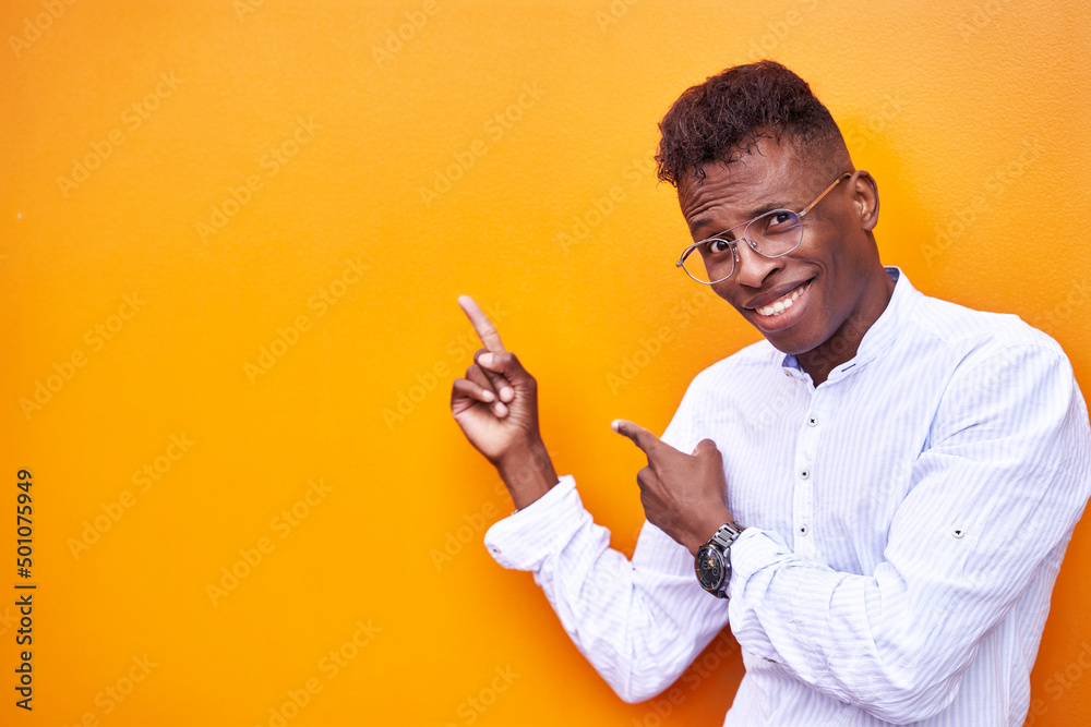 African American businessman in smart shirt and glasses on orange background isolated smiling and looking at camera pointing with both hands and fingers to one side. High quality photo