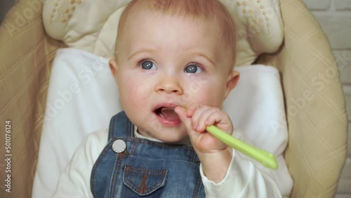 baby girl chews plastic spoon and looks at camera, zoom in