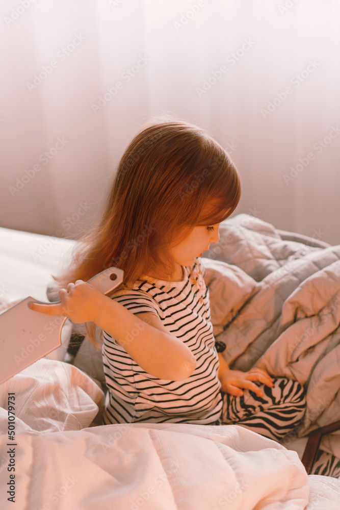 Cute toddler girl sitting on bed with brush and mirror.