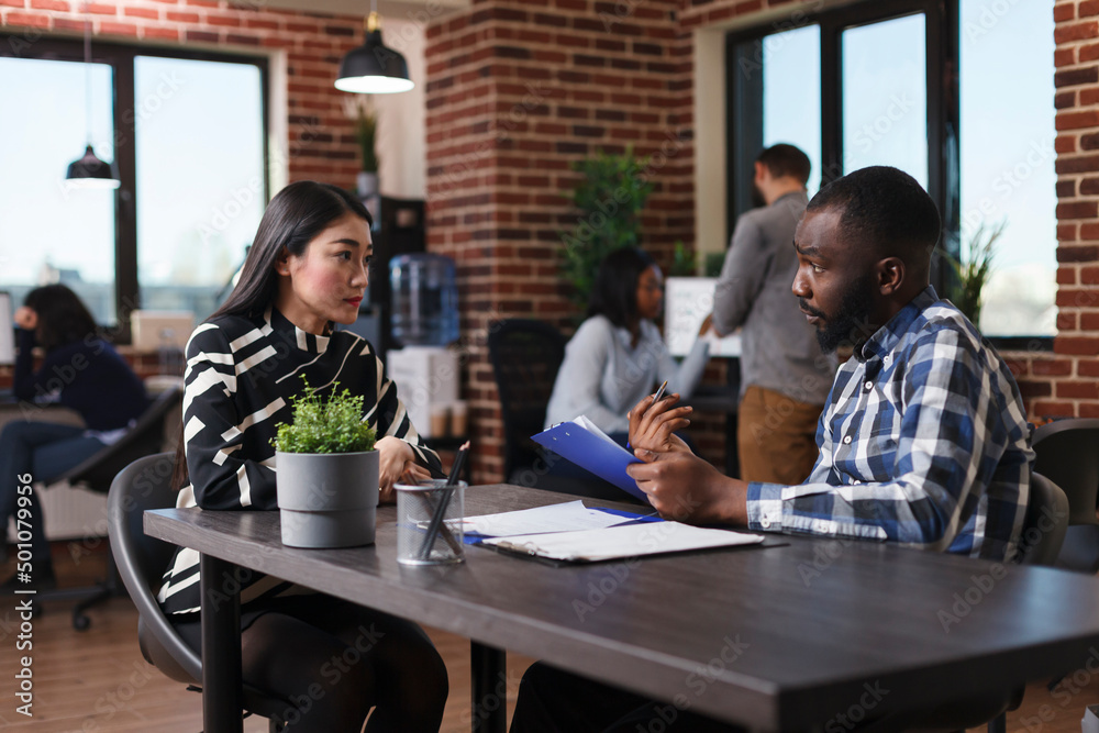 Asian woman arrived for interview sitting at desk in office while talking with business company recruiter about job description. Executive manager presenting applicant salary offer and ways of work