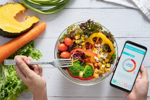 Calories counting , diet , food control and weight loss concept. Calorie counter application on smartphone screen at dining table with salad, fruit juice, bread and fresh vegetable. healthy eating