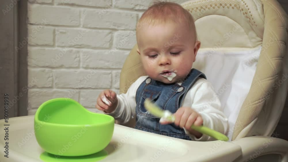 baby sits in chair and plays with spoon smeared with yogurt baby sits in chair and plays with spoon smeared with yogurt