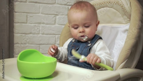 baby sits in chair and plays with spoon smeared with yogurt