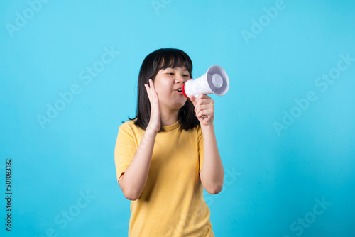 Happy Asian girl holding and talk on megaphone on blue background.