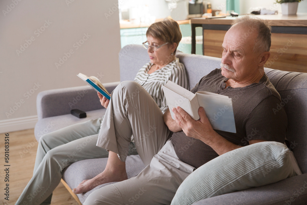 Fototapeta premium healthy seniors lifestyle. spend free time do favourite hobby. elderly couple reads books sitting on the couch at home