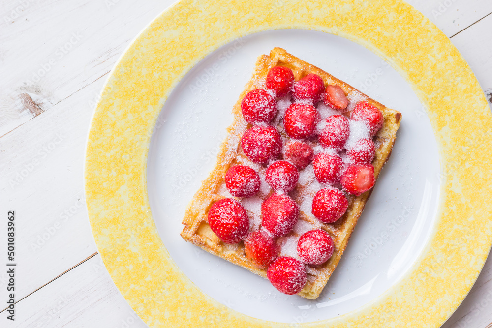 Warm Belgian waffle with fresh strawberries and suger on a plate with copy space Warm Belgian waffle with fresh strawberries and suger on a plate with copy space