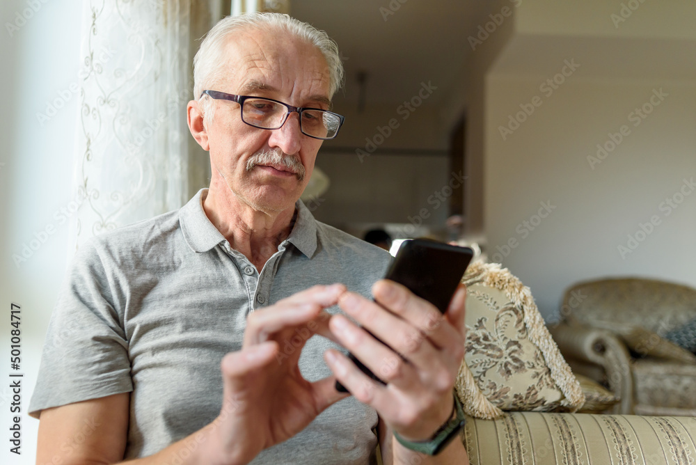 Senior man in eyeglasses using mobile phone at home Senior man in eyeglasses using mobile phone at home
