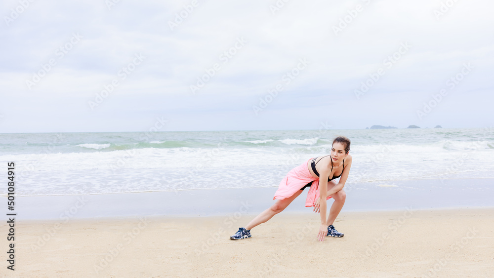 asian woman in sport wear and pink jacket exercise on the beach at evening in the rain season