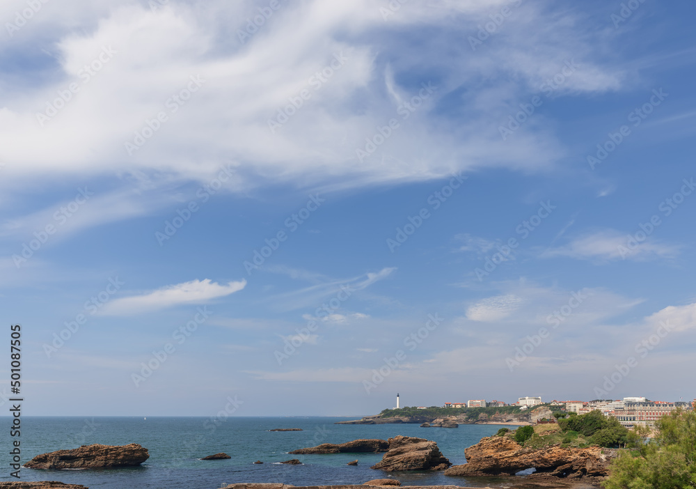 Sea surface of Biscay Bay, rocks formed by it, the Biarritz coastal line with a lighthouse. Biarritz, French Basque Country