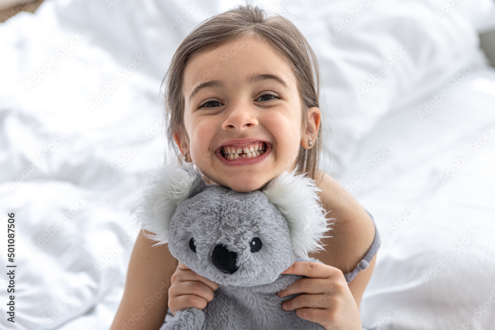 Happy little girl with soft toy koala in bed.