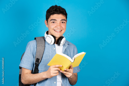 Portrait of hispanic college student holding a book isolated on blue background.