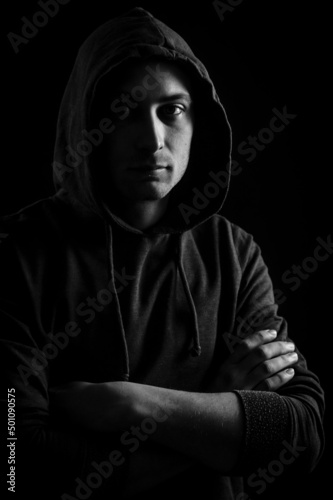 Black and white portrait of a handsome young blue-eyed hooded man with his arms crossed