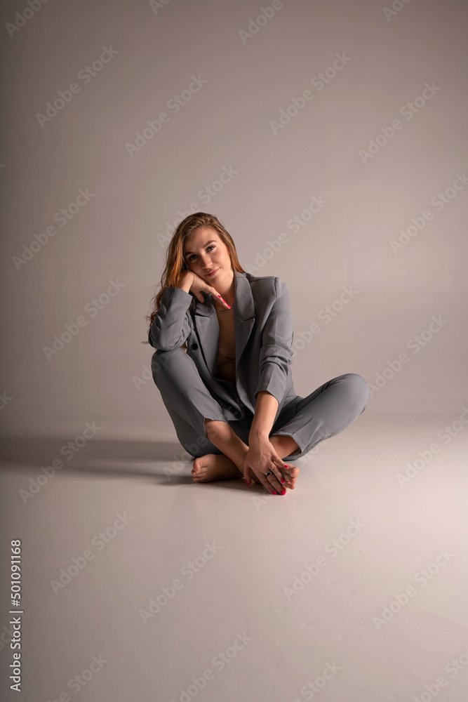 A beautiful blonde girl in a pantsuit with an unbuttoned jacket from under which a beautiful slender sexy body and underwear can be seen posing on a white background sitting on the floor and smiling A beautiful blonde girl in a pantsuit with an unbuttoned jacket from under which a beautiful slender sexy body and underwear can be seen posing on a white background sitting on the floor and smiling