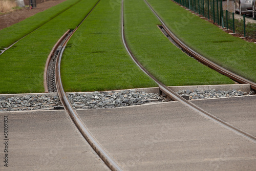 the railway turns on the bitumen and continues on very green grass. The rails pass on the road then stone to finish on green grass guiding the gaze.