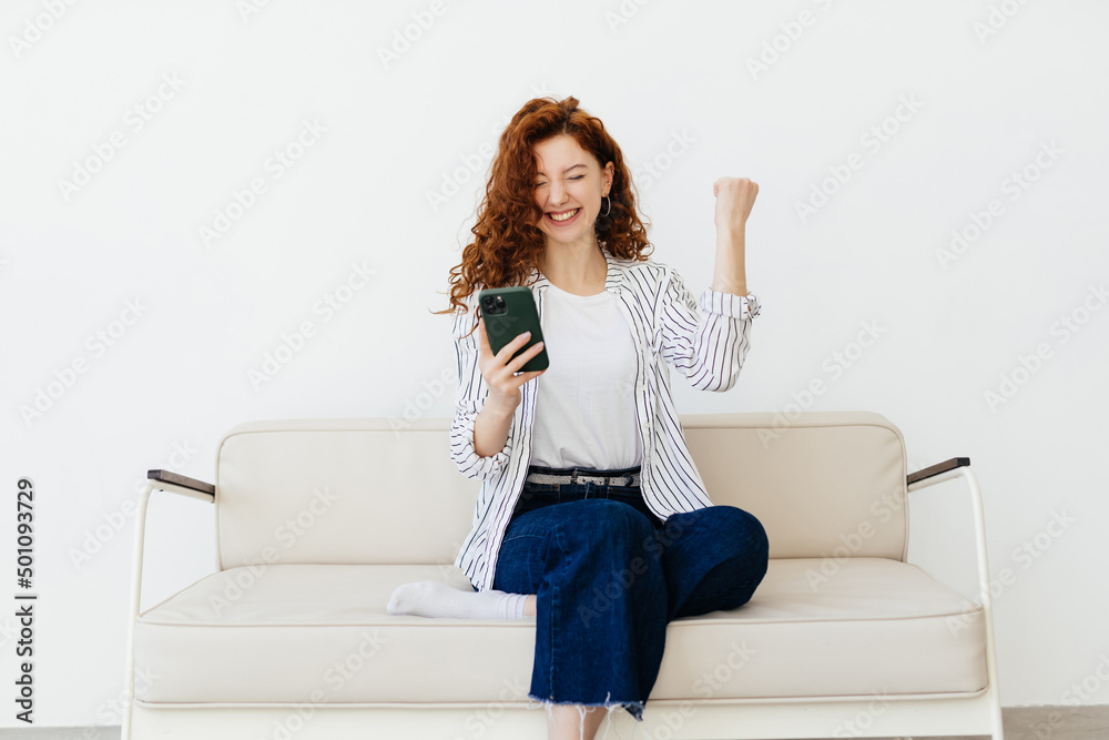 Yes. Portrait of lucky cheerful woman holding and using her cell phone, shaking fist, screaming yeah, celebrating win or victory, playing games online, reading great news, sitting on couch