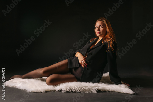 Obraz na plátně A luxurious half-naked blonde in sexy underwear and an unbuttoned black jacket lies seductively in the semi-darkness on the skin (fur) of a polar bear
