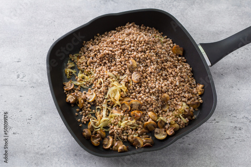 Non-stick frying pan with buckwheat, fried onions and champignon mushrooms on a gray textured concrete background, homemade food. Cooking a traditional Jewish dish kasha varnishkes photo